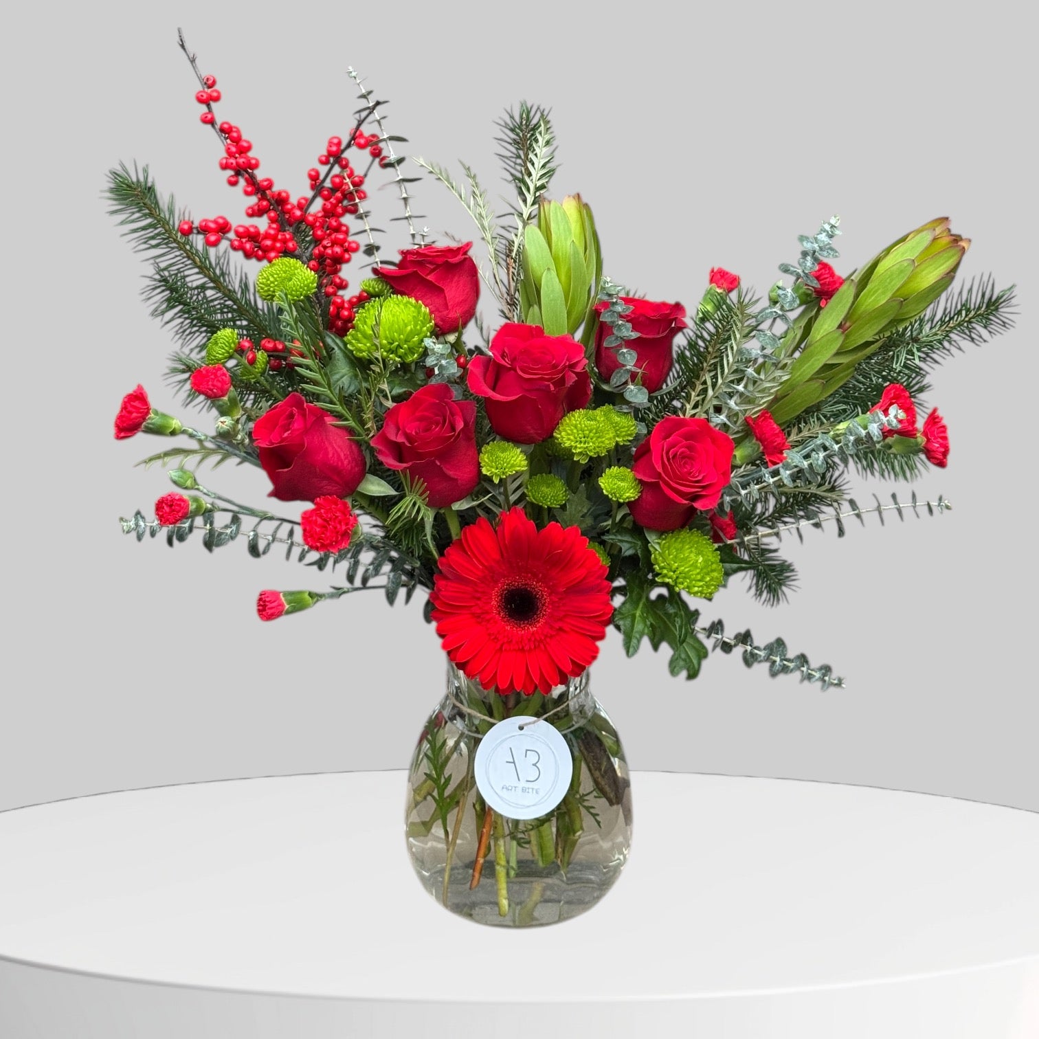 Deep red holiday flower arrangement in a vase with seasonal greenery